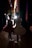 Two young ballerinas stand backstage, dressed in elaborate tutus and ballet shoes, facing a brightly lit stage. The setting conveys anticipation as they wait to perform. The lighting creates a dramatic silhouette effect, emphasizing their poised posture and elegant costumes.