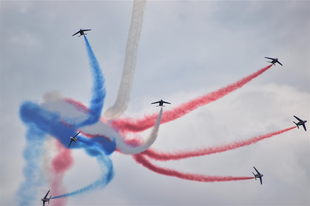 a group of airplanes flying in formation with red and blue smoke behind them