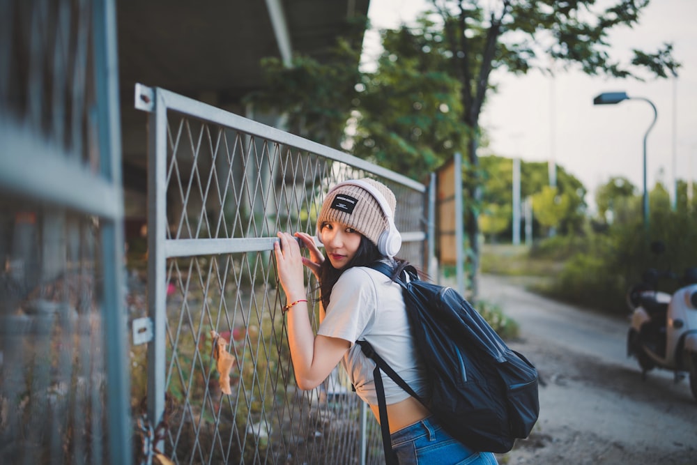 eine frau mit rucksack, die an einen zaun lehnt