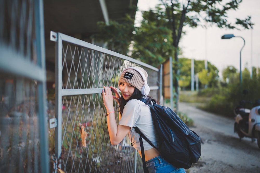 a woman with a backpack leaning against a fence