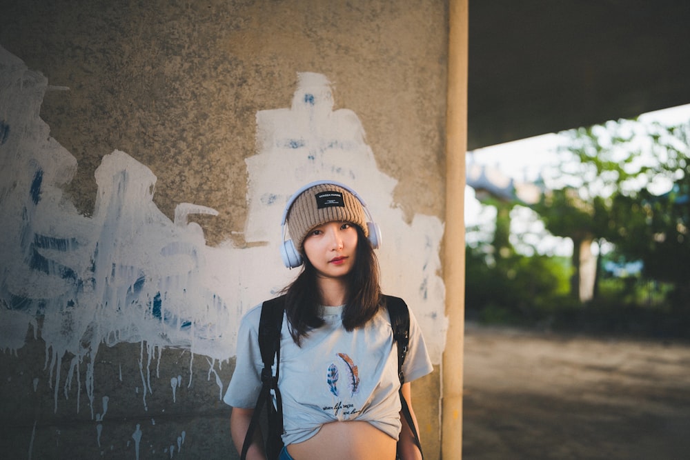 a woman with a backpack and a hat standing in front of a wall