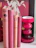 Several vintage books with red and pink covers are neatly arranged vertically on a white surface. Next to the books is a glossy red candle holder or decorative vase with a modern design. In the background, there is part of a poster featuring an individual holding what appears to be stalks of wheat.