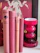 Several vintage books with red and pink covers are neatly arranged vertically on a white surface. Next to the books is a glossy red candle holder or decorative vase with a modern design. In the background, there is part of a poster featuring an individual holding what appears to be stalks of wheat.