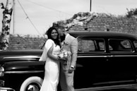 A groom in a traditional yet contemporary designer suit standing beside a vintage car.