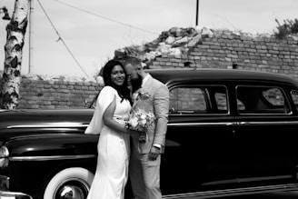 A groom in a traditional yet contemporary designer suit standing beside a vintage car.