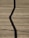 A wooden deck surface with a prominent zigzag shadow cast across it. Long, straight planks create a lined texture, and some small twigs or debris are scattered randomly.