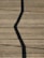 A wooden deck surface with a prominent zigzag shadow cast across it. Long, straight planks create a lined texture, and some small twigs or debris are scattered randomly.