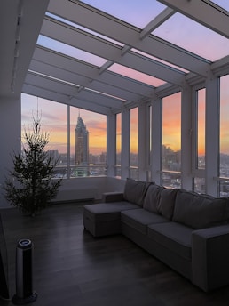 A cozy modern living room with large windows overlooking a city skyline at sunset.