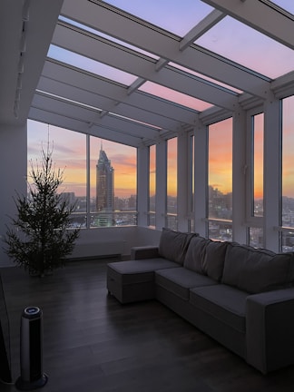 Bright, modern living room with floor-to-ceiling windows overlooking a city skyline at sunset.