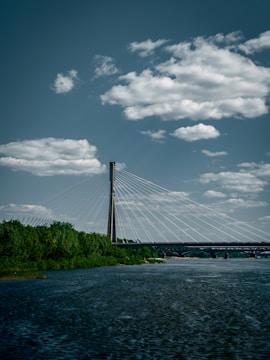 A long suspension bridge spanning a wide river with lush greenery on both banks.