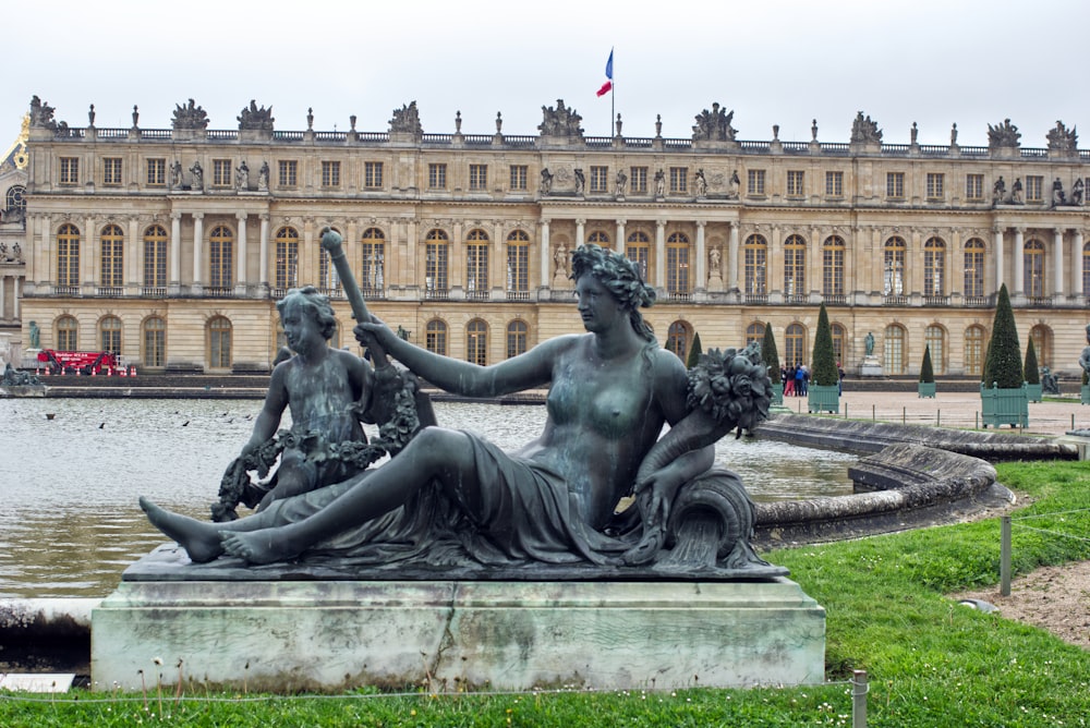 a statue in front of a building with a fountain in front of it