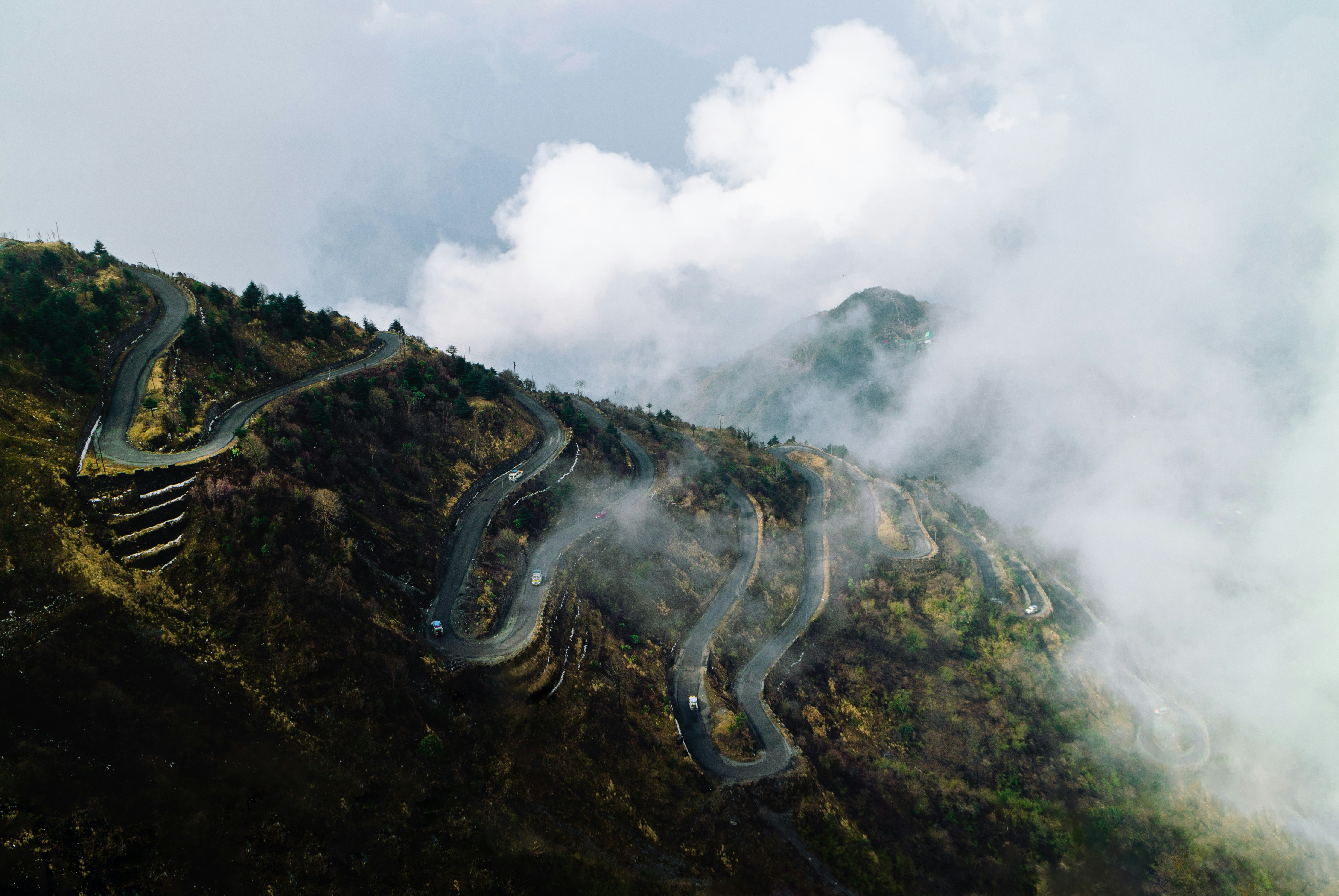 a long winding road on a mountain side, Beautifully curving roads with clouds rolling over as seen on the Himalayan hills in Zuluk, East Sikkim