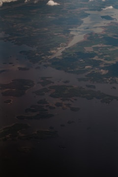 An aerial view of a landscape featuring a network of waterways and patches of land. The image shows various small islands surrounded by a large body of water. Scattered clouds cast shadows on the surface below, while different shades of green and brown indicate forested and open land areas.