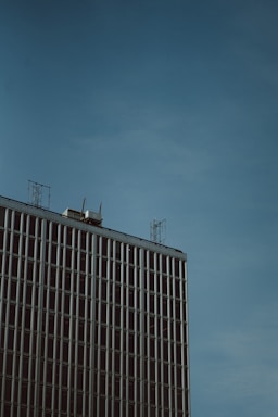 A sleek, modern office building in Dubai with telecom antennas on the rooftop under a clear blue sky.