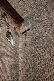 A tall brick wall with intricate patterns and several arched windows. The architecture includes decorative elements and grills on some of the windows, showcasing detailed masonry work.