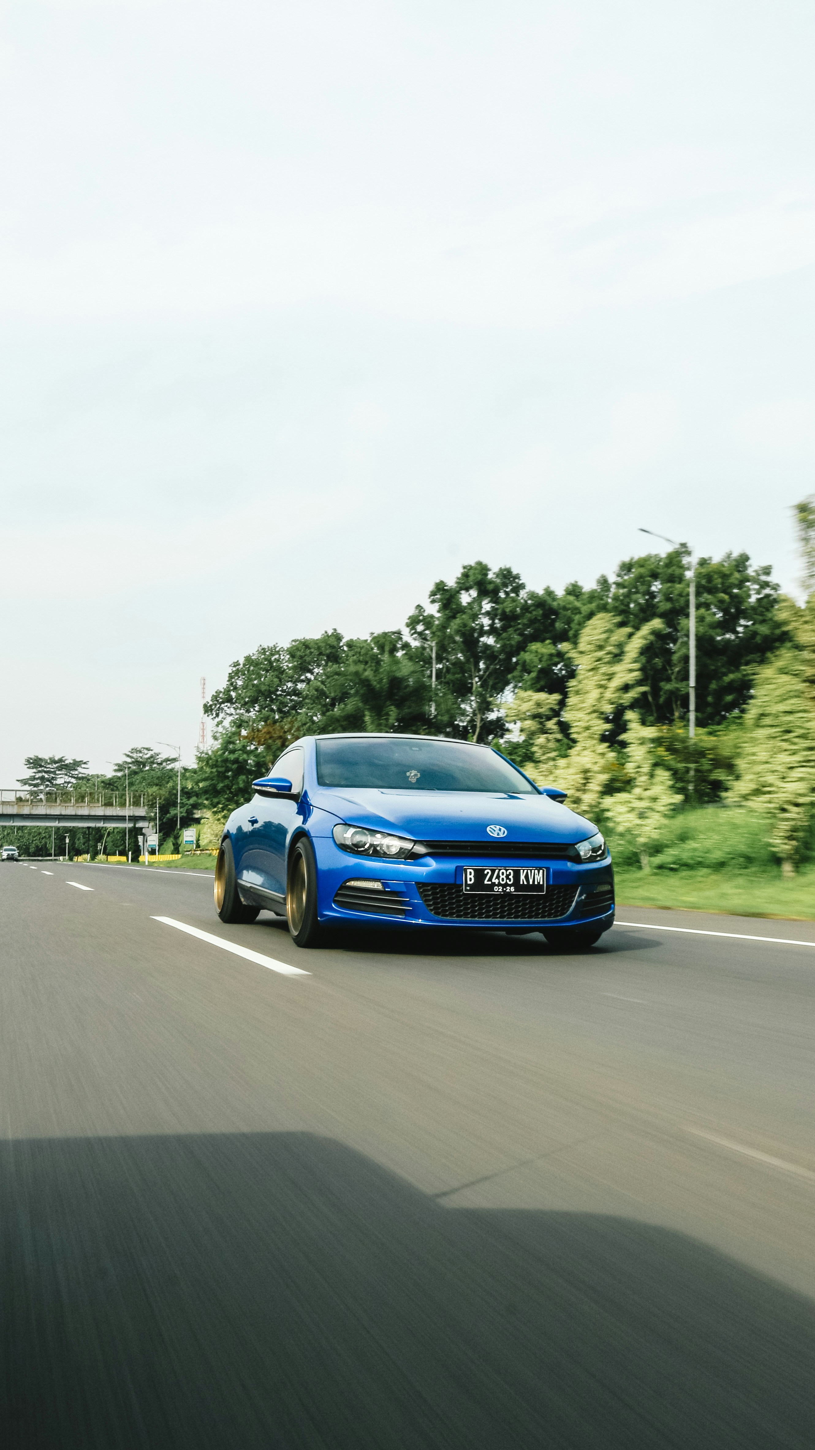 a blue car driving down a road next to a forest