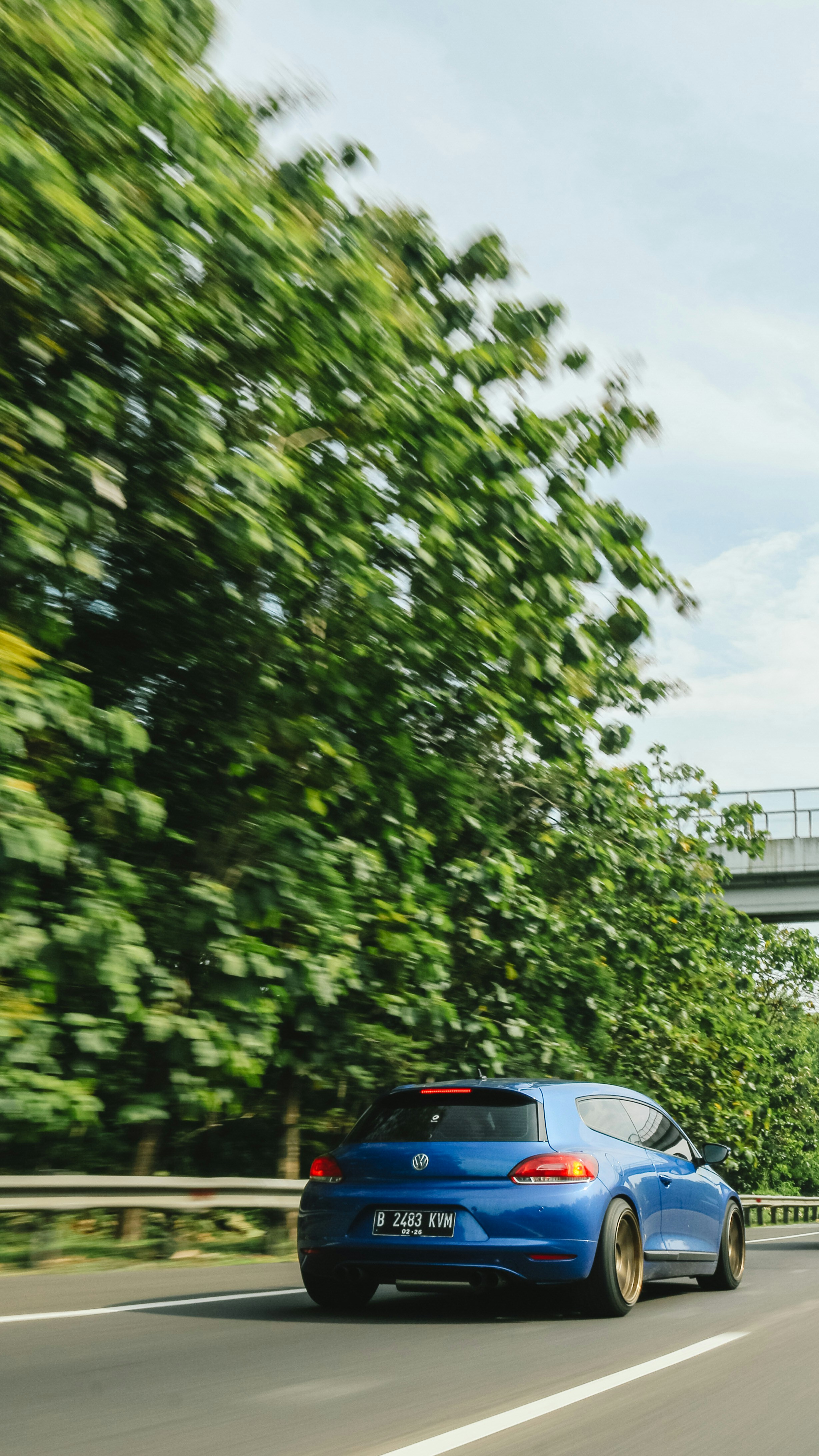 a blue car driving down a road next to a bridge