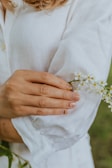 Close-up of manicured hands with nude polish holding a delicate flower.