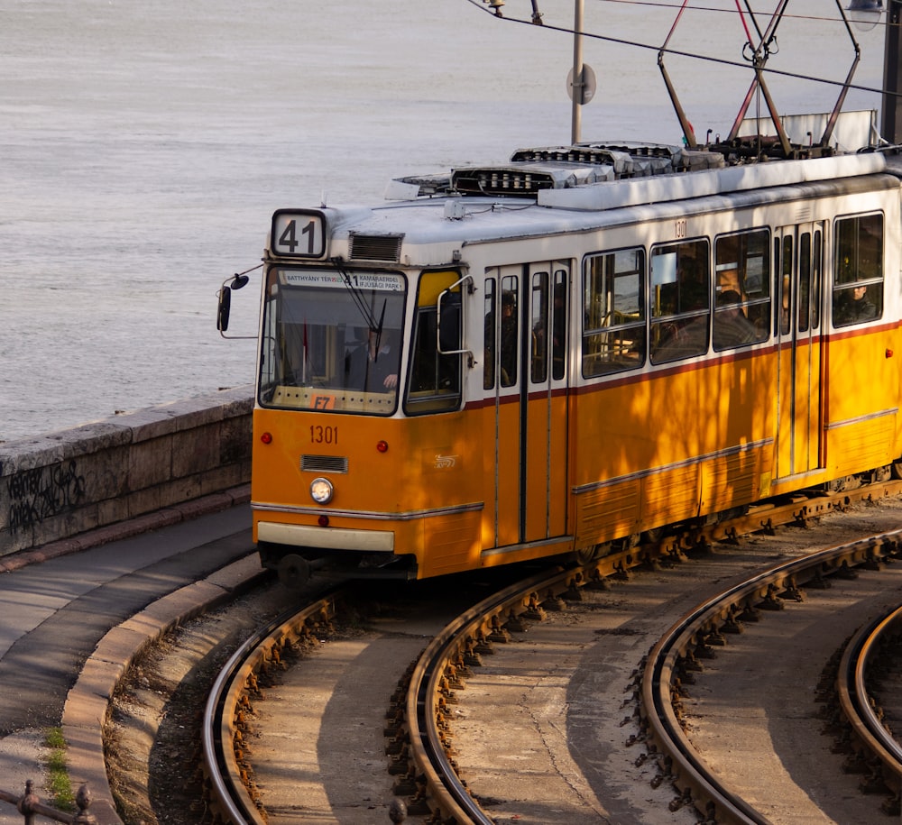 a yellow trolley car traveling down tracks next to a body of water