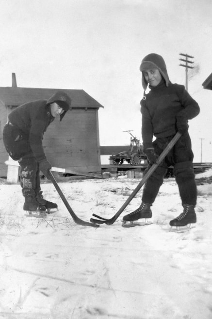 Children playing hockey on the rink, wearing colorful jerseys and smiling.