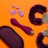 An arrangement of objects on an orange background includes purple handcuffs with a furry texture, a purple ergonomic device, a purple pouch, and several purple plastic bricks resembling toy blocks.