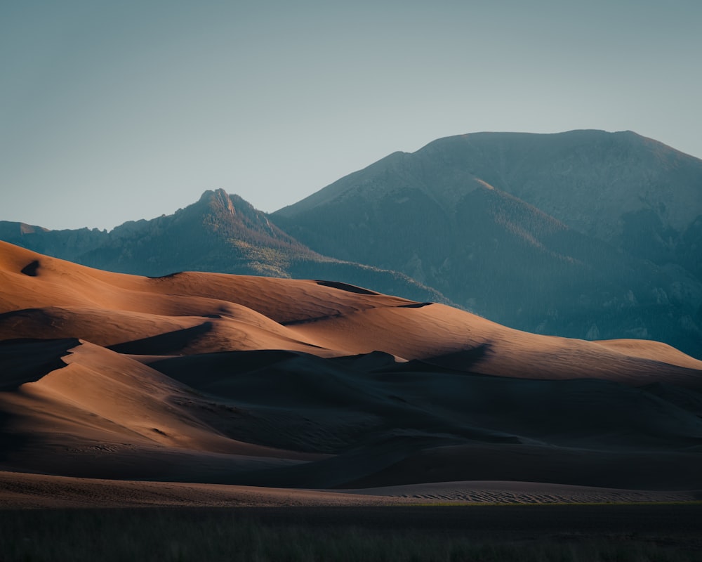 a mountain range in the distance with sand dunes in the foreground