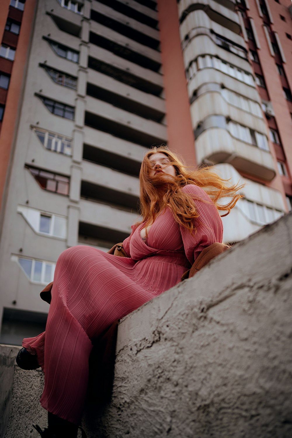 a woman in a pink dress sitting on a ledge in front of a tall building