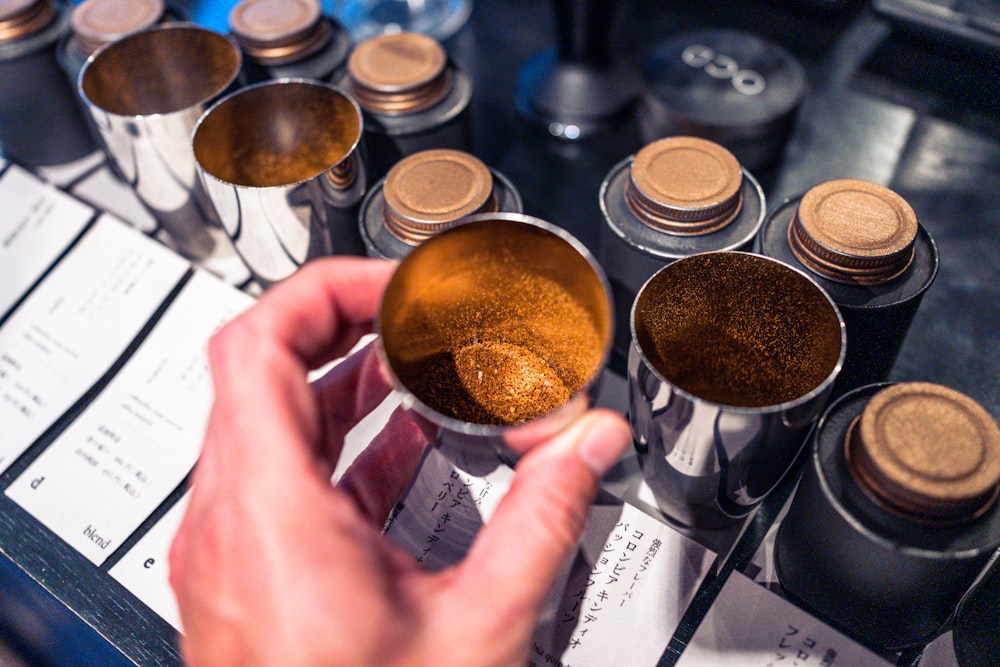 a person holding a spoon over a table full of spices