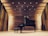 A grand piano and bench are placed on a wooden stage inside a concert hall. The walls and ceiling are composed of wooden panels with spotlights illuminating the area.