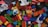 A scattered collection of colorful building blocks and toy pieces, featuring various shapes and sizes. Some blocks have illustrations of animals and are interspersed with small toy figures. The toys are placed on a textured dark surface.