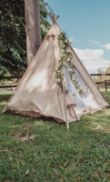 a teepee is set up in the grass near a tree