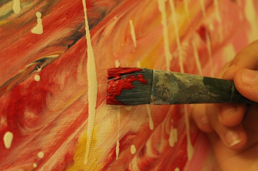 A close-up photo of Sandra's hands painting a vibrant abstract canvas in her college studio.