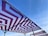 Geometric-patterned canopies with maroon and white zigzag designs are stretched over metal frames against a clear blue sky.