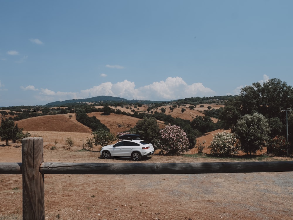 a white car parked in a field next to a wooden fence