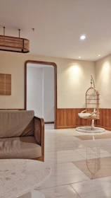 A modern, minimalistic interior space featuring a beige and brown color palette. The room includes a hanging rattan chair and a sofa with wooden accents. The floor is polished and reflective, and the walls have a combination of light and dark wooden panels. A stylish light fixture hangs from the ceiling.