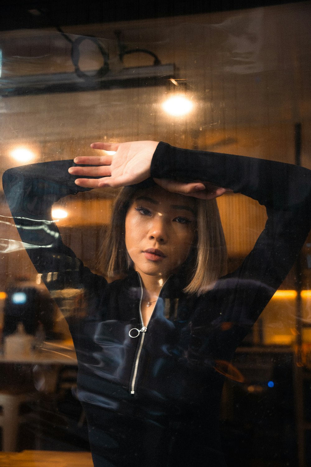 a woman standing in front of a window with her hands on her head