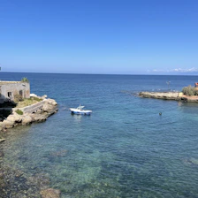 A sleek boat anchored near a rocky coastline with turquoise sea and blue sky