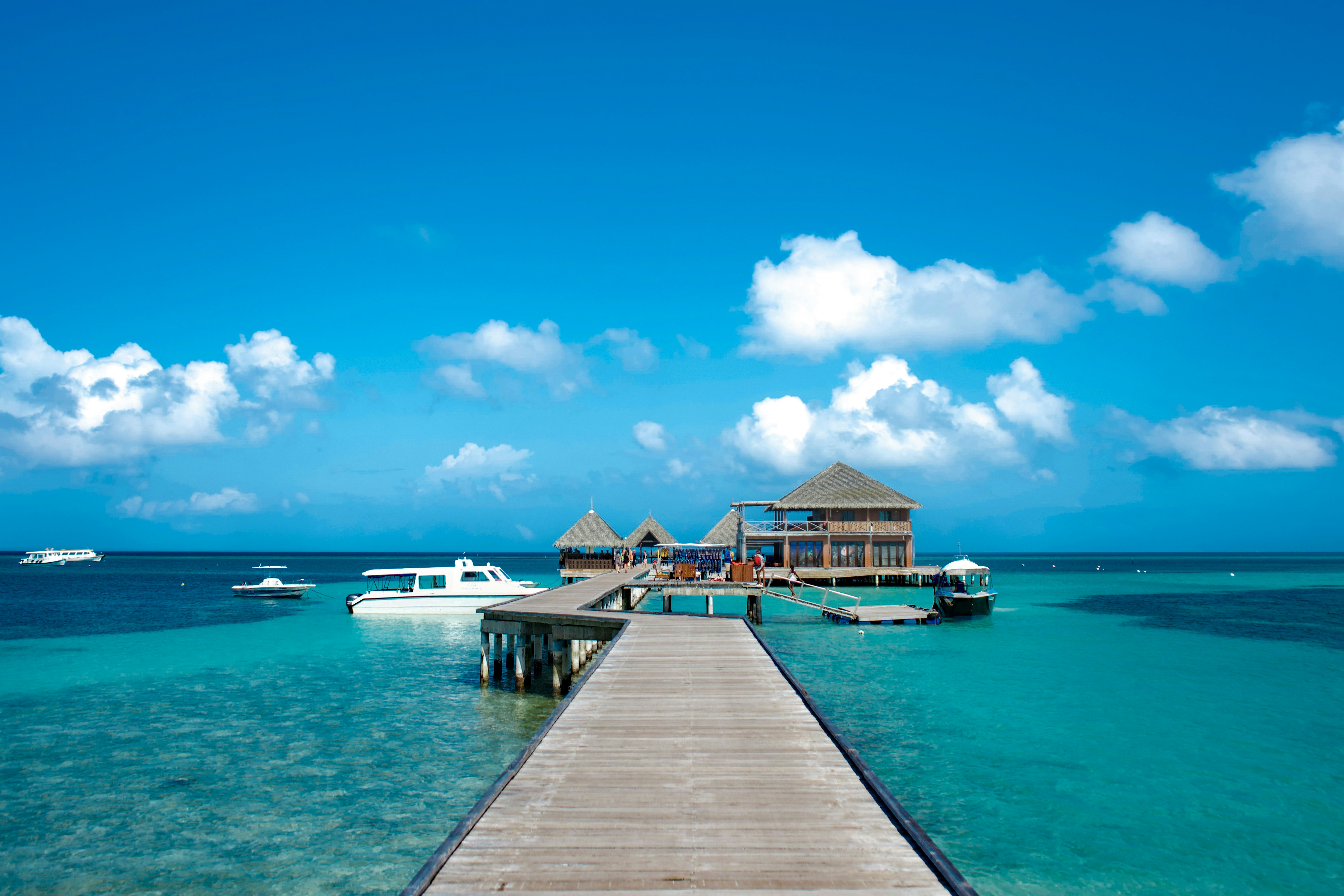 a pier leading to a beach with boats in the water, Jetty of a Maldivian island.