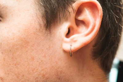 A close-up view of a human ear adorned with a small hoop earring. The image captures the texture of the skin and the contours of the ear. Hair is visible, and the lighting highlights the skin tones.