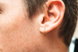 A close-up view of a human ear adorned with a small hoop earring. The image captures the texture of the skin and the contours of the ear. Hair is visible, and the lighting highlights the skin tones.