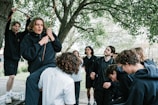 A group of young people gathered outdoors, engaged in a lively community discussion under a large tree.