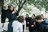 Youth leaders engaged in an outdoor mentorship session under a large, shady tree.