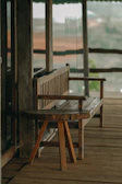 A rustic wooden bench stool with a soft cushion placed on a porch.