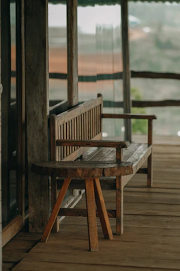 A rustic wooden bench stool with a soft cushion placed on a porch.