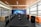 A modern conference room features a long black table surrounded by leather chairs with high backs. On one side, large windows allow natural light to fill the space. The opposite wall displays a mural of a world map with digital network graphics. Orange sofas are placed along the windows, adding a pop of color.