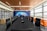 A modern conference room features a long black table surrounded by leather chairs with high backs. On one side, large windows allow natural light to fill the space. The opposite wall displays a mural of a world map with digital network graphics. Orange sofas are placed along the windows, adding a pop of color.
