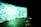 A large, curved screen displays vibrant, abstract patterns with dominant shades of blue and green, creating a surreal and immersive atmosphere. The room is dimly lit, enhancing the luminous effect of the screen. In the foreground, there are several round cushions placed on a concrete floor.