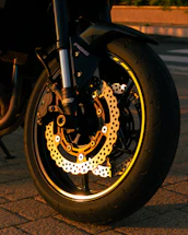 A close-up of a motorcycle wheel with shiny rims and brake pads under natural light.