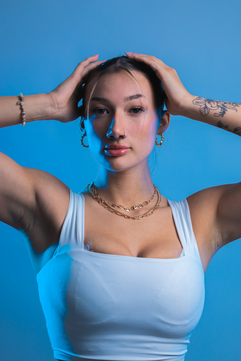 a woman in a white tank top holding her hands on her head