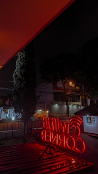 A bright neon box sign glowing at night outside a busy Surabaya shop.